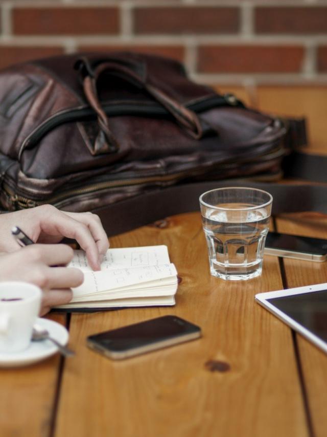 Friends Sitting In Cafe Writing In Notebook With Digital Tablet And Coffee Cup