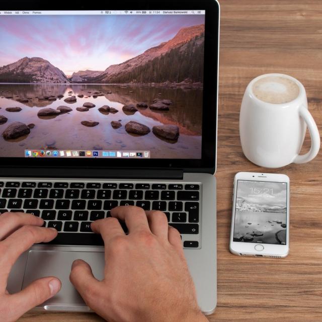 Man Sitting In Front Of Laptops Screen With Mountain Landscape On