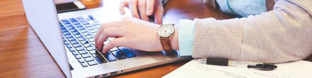 Woman Sitting At Table And Using Laptop With Tea Cup In Background