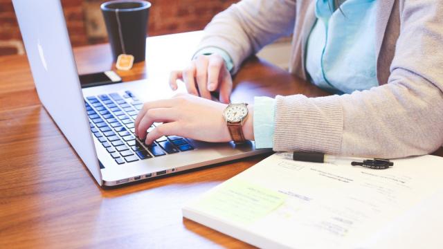 Woman Sitting At Table And Using Laptop With Tea Cup In Background