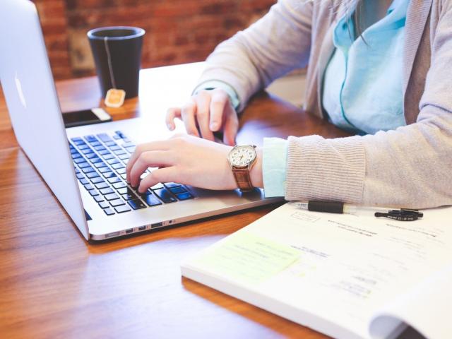 Woman Sitting At Table And Using Laptop With Tea Cup In Background