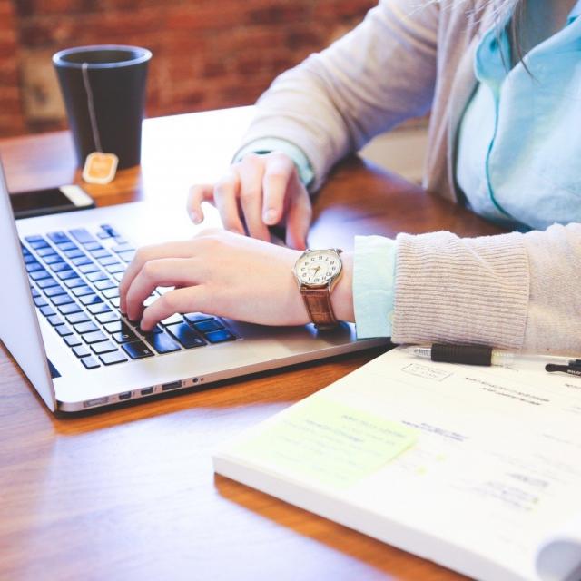 Woman Sitting At Table And Using Laptop With Tea Cup In Background