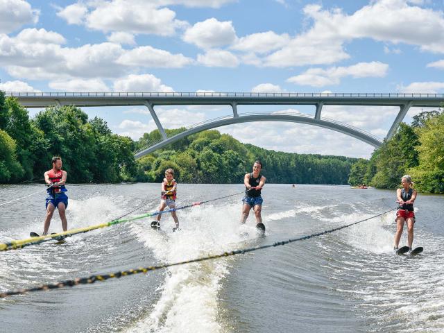 4 personnes font du ski nautique sur la Mayenne, tractées par le même bateau. En arrière plan on voit le nouveau viaduc de Château-Gontier