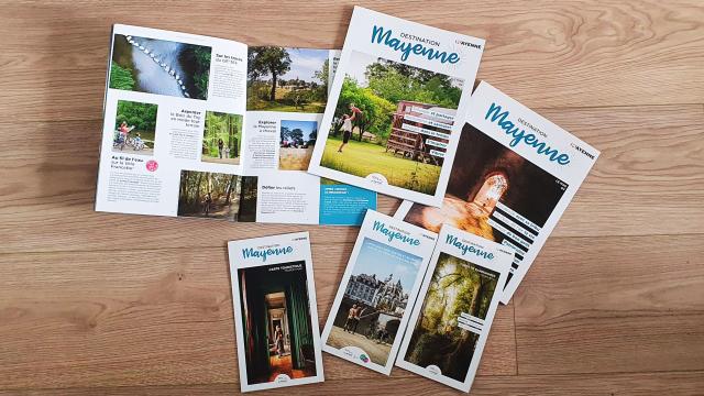 les magazines et les cartes touristiques de Mayenne tourisme sont disposées sur un fond en bois.